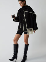 Model draagt zwarte cape met franjes
