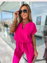 vrouw in roze jumpsuit met clutch en zonnebril
